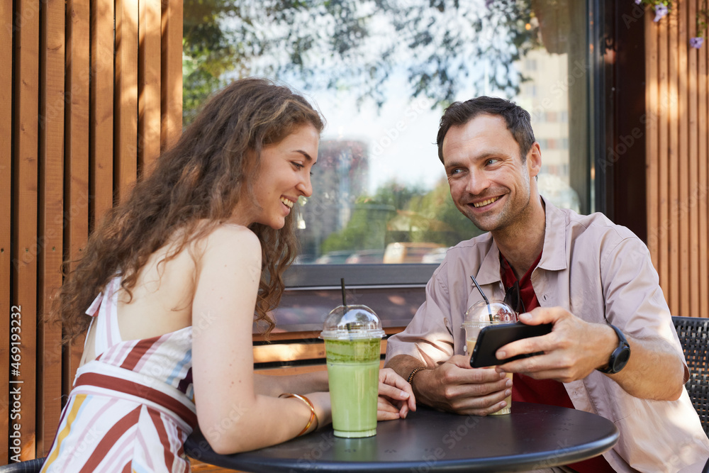Portrait of happy couple looking at smartphone screen at outdoor cafe while enjoying date in Summer, copy space Portrait of happy couple looking at smartphone screen at outdoor cafe while enjoying date in Summer, copy space