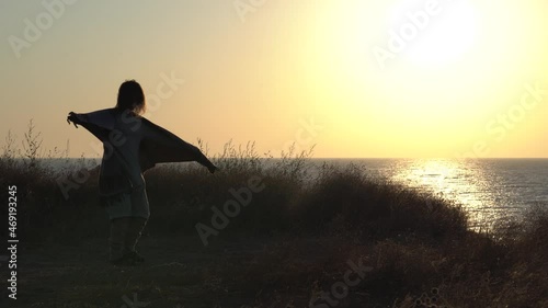 Young woman meditates, dances and whirls at sunrise, sunset on the seashore. Silhouette of a woman, meditation, relaxation, vacation, travel, seascape. Yoga classes in the rays of the sun. 4K video.