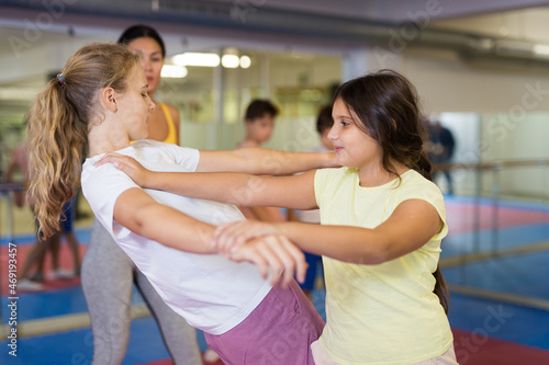 Pair of teenager school girls practicing new self-defense moves during training in gym photo