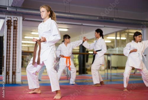 Sportive girl in kimono standing in combat stance and posing while other kids training behind her.