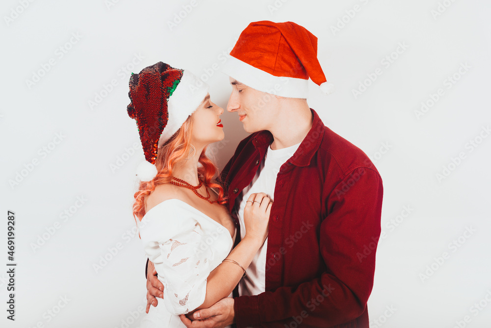 Obraz premium Couple in red santa hats on a white background laugh and celebrate new year and christmas. Couple kissing in new year.