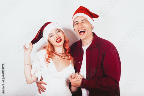 Couple in red santa hats on a white background laugh and celebrate new year and christmas. Little girl with pink hair and white dress laughs