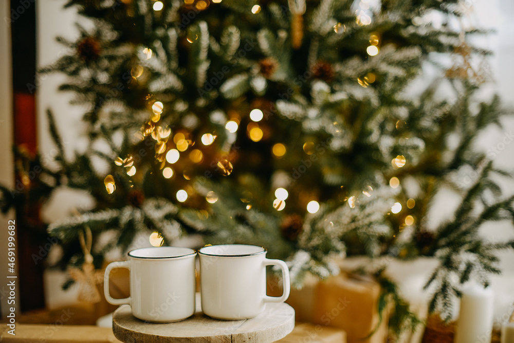 Fototapeta premium New year 2022, christmas. House room decorated for the holidays. Two cups of tea or coffee on the background of the Christmas tree. Christmas drinks. Warmth and comfort