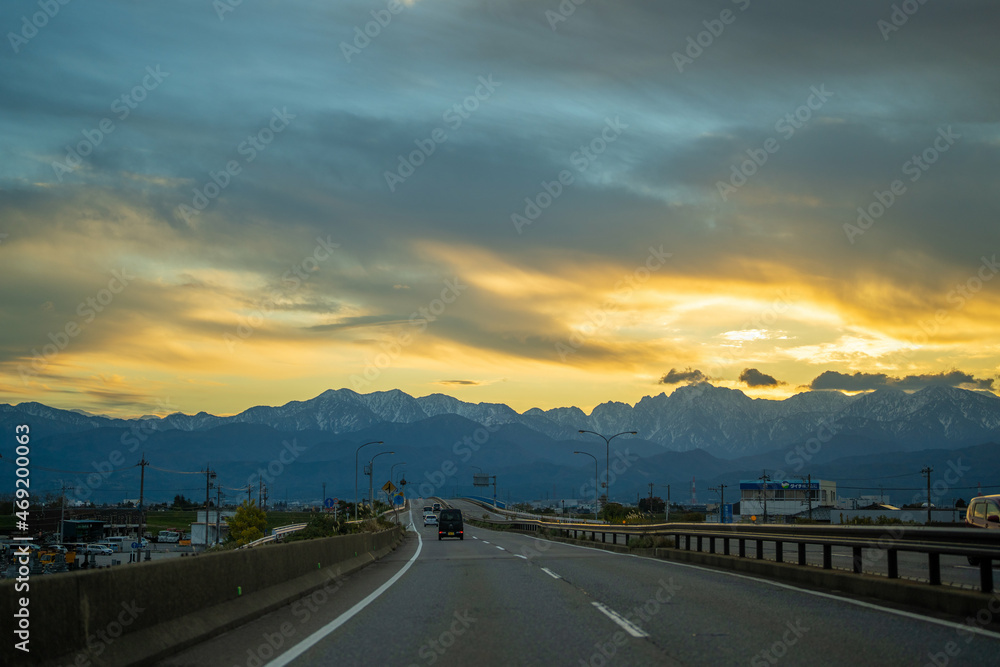 Fototapeta premium 富山県富山市の道路から朝焼けの剱岳や立山を見る風景 View of Tsurugidake and Tateyama in the morning sun from the road in Toyama City, Toyama Prefecture, Japan.