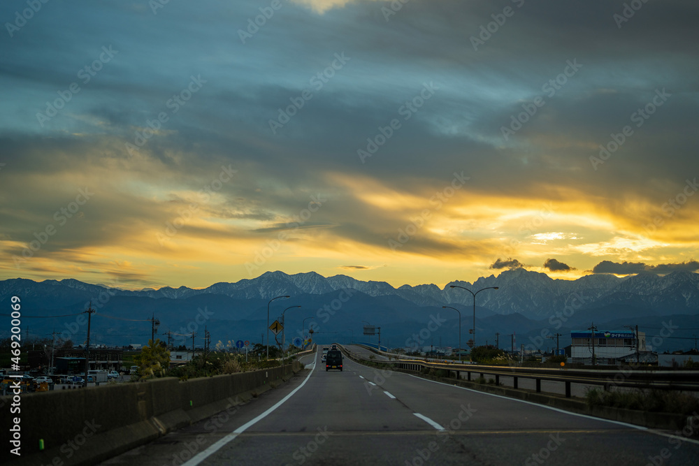 Fototapeta premium 富山県富山市の道路から朝焼けの剱岳や立山を見る風景 View of Tsurugidake and Tateyama in the morning sun from the road in Toyama City, Toyama Prefecture, Japan.
