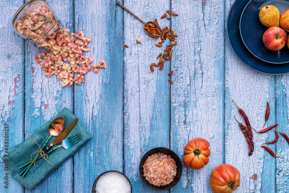 Still life with iridescent metal forks, himalayan salt, colored pasta, tomatoes and peppers on blue wooden background Still life with iridescent metal forks, himalayan salt, colored pasta, tomatoes and peppers on blue wooden background