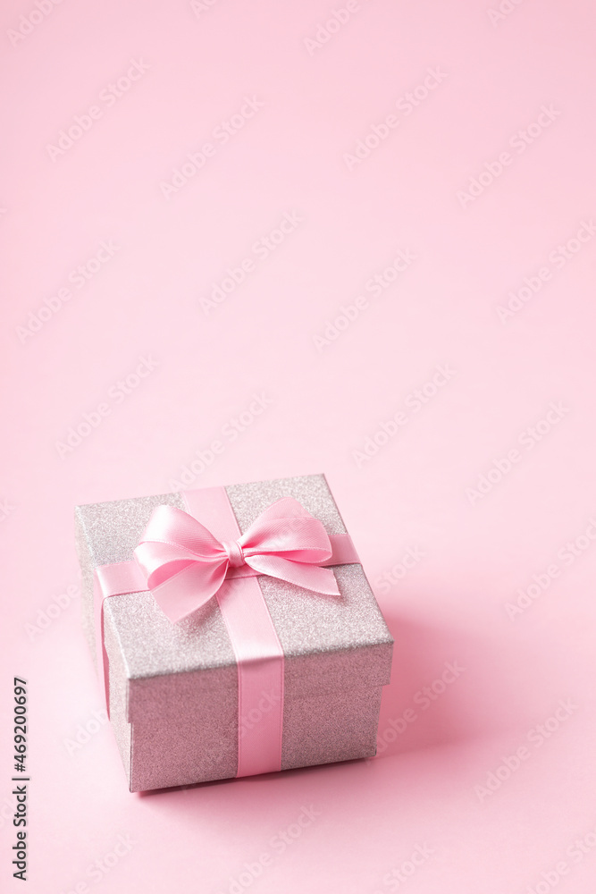 Silver glitter gift box with pink ribbon bow on pink background. Christmas, Valentine's day or birthday concept. Place for text. View from above.