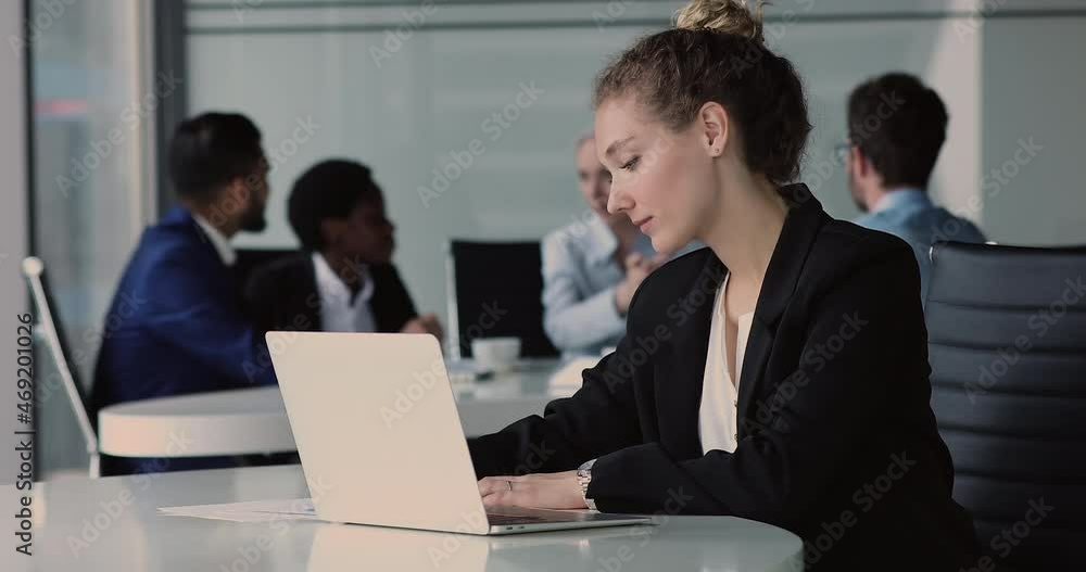 Young beautiful businesswoman sit at desk with laptop, writes notes, do sales analysis, work on-line, make forecast, looks focused, diverse employees on background. Modern tech, online project concept Young beautiful businesswoman sit at desk with laptop, writes notes, do sales analysis, work on-line, make forecast, looks focused, diverse employees on background. Modern tech, online project concept