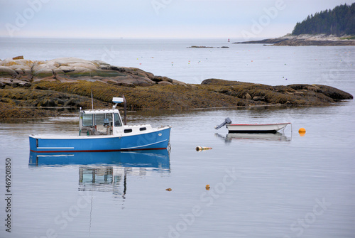 Tranquil scene in coastal Maine.  Blue lobster boat and small dinghy anchored alongside rocky outcrop near South Thomaston, Maine.