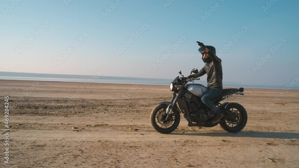 Motorcyclist driving his customized fast motorbike on the dirt road in desert around sea or lake Motorcyclist driving his customized fast motorbike on the dirt road in desert around sea or lake