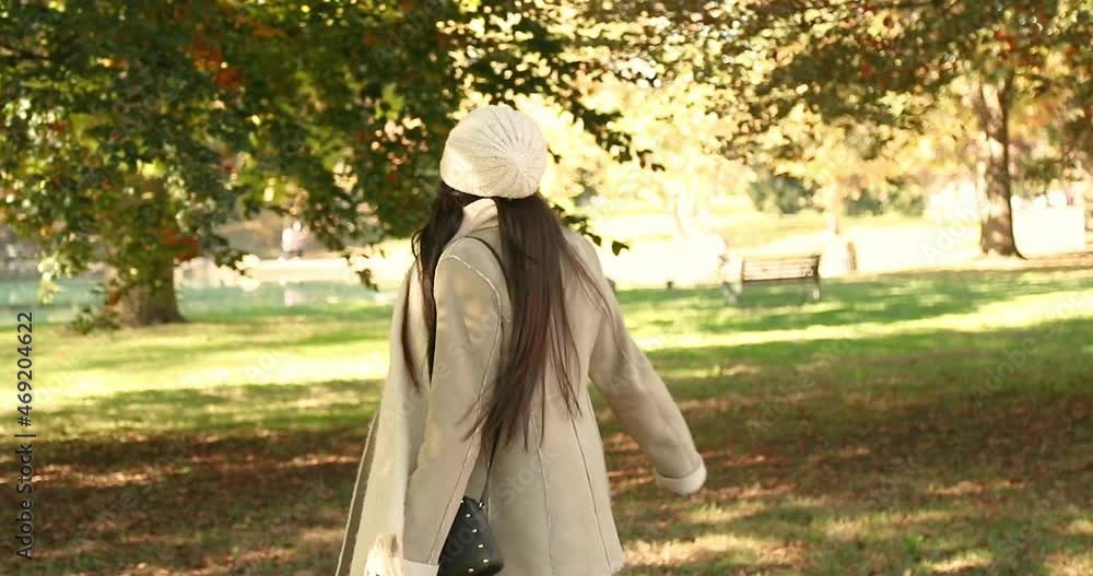Attractive girl looks and walks around at the chilly fall autumn leaves at a city park. She spins with her arms up and a big smile. She is wearing a white jacket and beanie. Shot in 4k slow motion Attractive girl looks and walks around at the chilly fall autumn leaves at a city park. She spins with her arms up and a big smile. She is wearing a white jacket and beanie. Shot in 4k slow motion