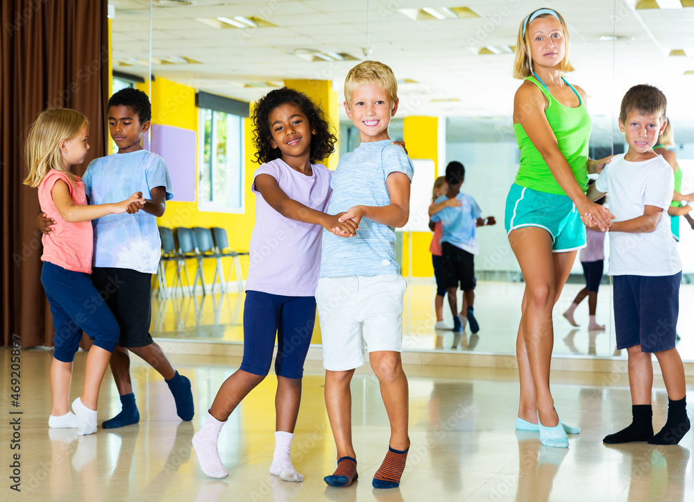 Happy tweens in pairs learning to dance waltz with female choreographer in modern studio