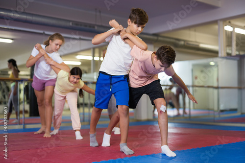 Kids exercising self-protection moves during group training in gym.