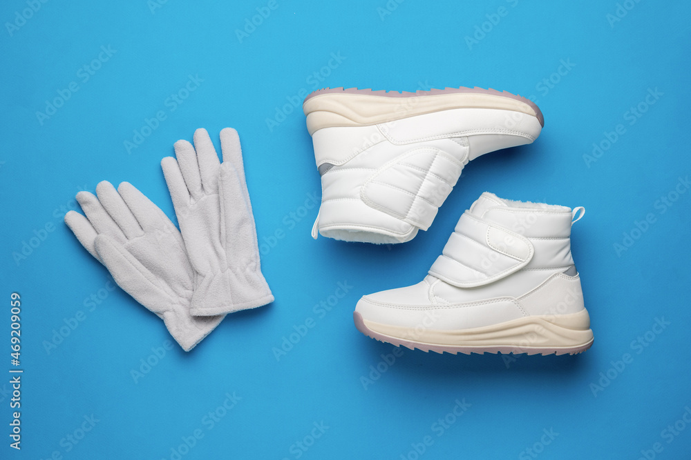 Grey gloves and white winter sneakers on a blue background. Flat lay. Grey gloves and white winter sneakers on a blue background. Flat lay.