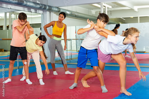 Focused kids in pair exercising self-defense movements during group class with female coach