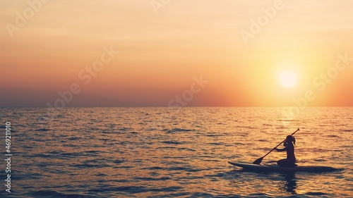 Silhouette of young woman playing paddle board in sea with the sunset sky background.Water sports concept And travel in the summer. © bunditinay