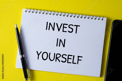 Selective focus of pen and notebook written with INVEST IN YOURSELF on yellow background. © youlanda