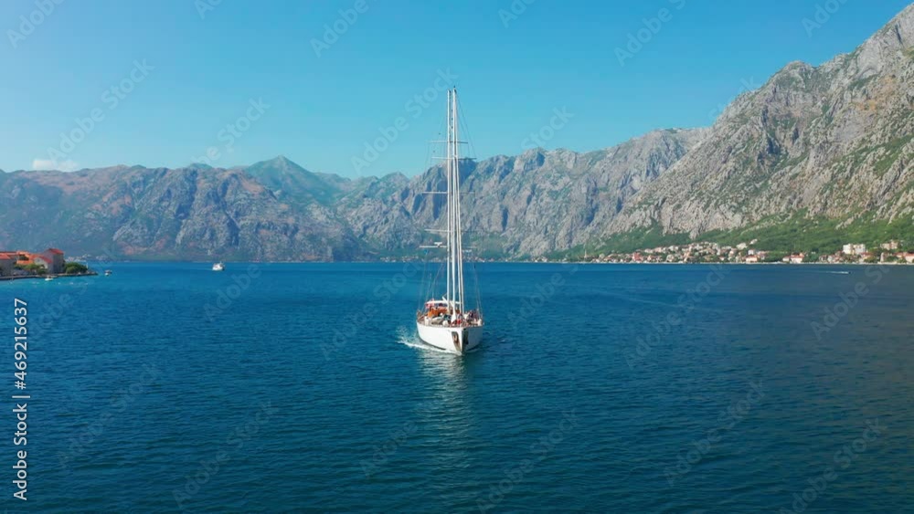 Sailing yacht in the Bay of Kotor with beautiful summer landscape of the coastline and mountains on background. Aerial drone view 4K. Sailing yacht in the Bay of Kotor with beautiful summer landscape of the coastline and mountains on background. Aerial drone view 4K.