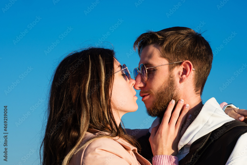 Candid portrait of two young lovers walking outdoors on sunny day. Guy and girl spend time together posing against backdrop bright blue sky. Concept of youth, love and lifestyle. Candid portrait of two young lovers walking outdoors on sunny day. Guy and girl spend time together posing against backdrop bright blue sky. Concept of youth, love and lifestyle.