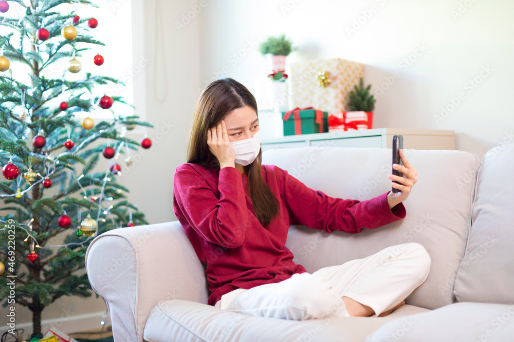 Young Asian woman wearing face mask sitting on the sofa, tired, feeling ill and headache. sickness during holiday season. Young Asian woman wearing face mask sitting on the sofa, tired, feeling ill and headache. sickness during holiday season.