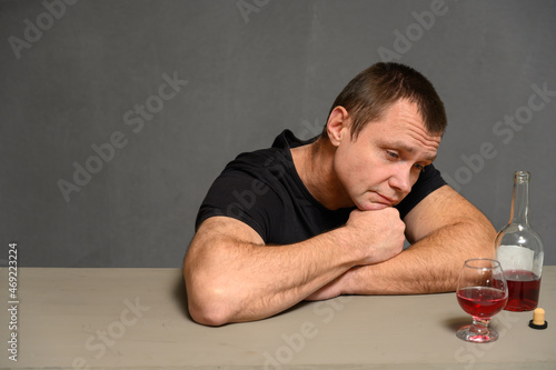 Photo man looks with a smile at the bottle of alcohol while sitting at the table