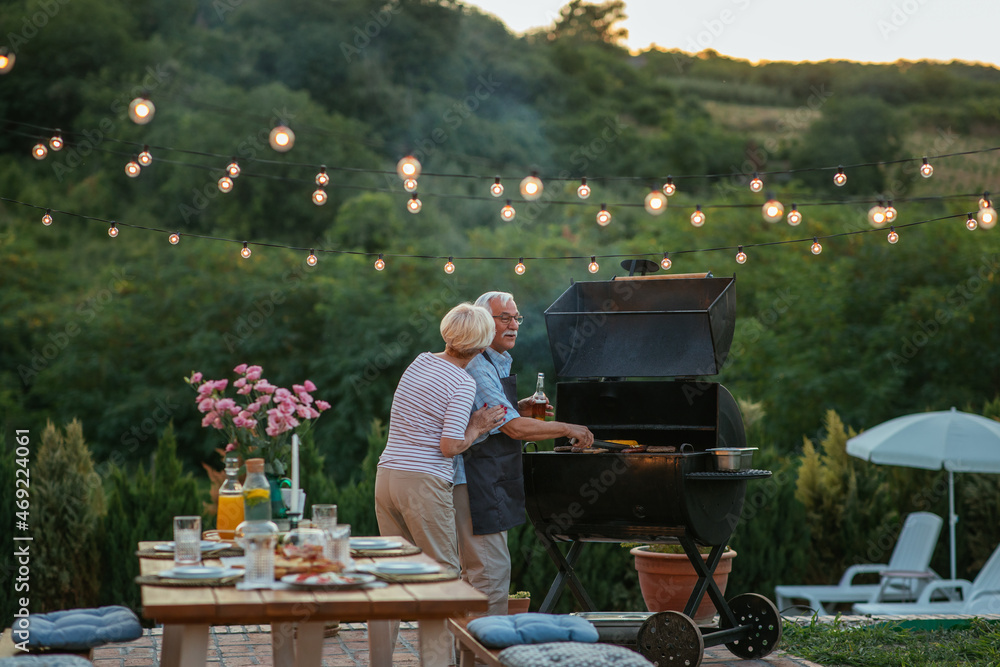 Senior woman makes a company to her husband who barbecuing in the backyard Senior woman makes a company to her husband who barbecuing in the backyard