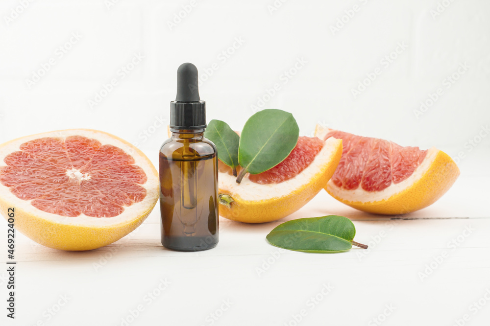 facial serum in a glass bottle with a pipette, ripe grapefruit and fruit slices on a white wooden background. facial serum in a glass bottle with a pipette, ripe grapefruit and fruit slices on a white wooden background.