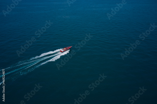 Top view of a red fast boat. Red speed boat fast movement on the water top view. Travel - image. Diagonal boat movement on blue water top view. © Berg