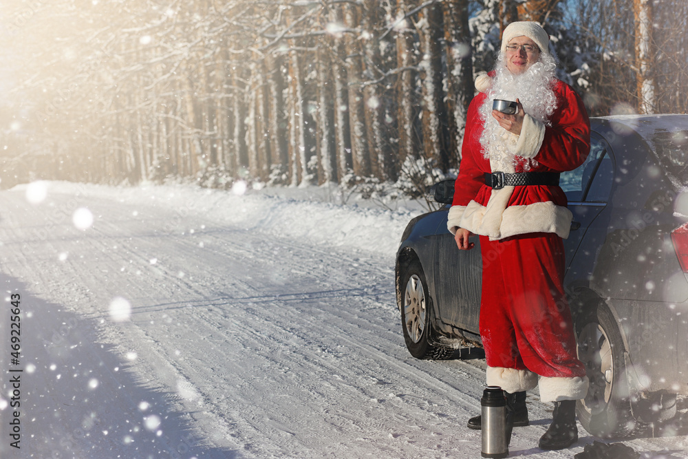Santa Claus comes with gifts from the outdoor. Santa in a red suit with a beard and wearing glasses is walking along the road to Christmas. Father Christmas brings gifts to children.