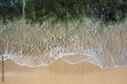 Aerial drone view in abstract mode of waves crashing along the shoreline of a white sand beach with turquoise clear lagoon water.