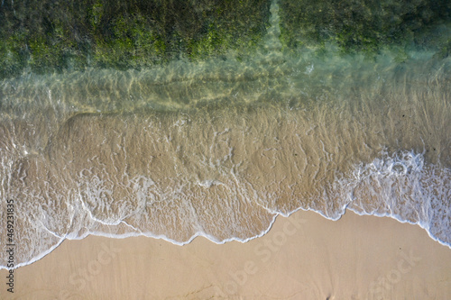 Aerial drone view in abstract mode of waves crashing along the shoreline of a white sand beach with turquoise clear lagoon water.