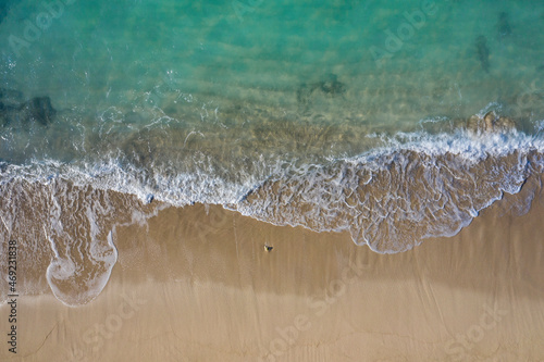 Aerial drone view in abstract mode of waves crashing along the shoreline of a white sand beach with turquoise clear lagoon water.