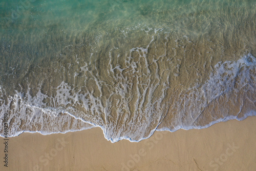 Aerial drone view in abstract mode of waves crashing along the shoreline of a white sand beach with turquoise clear lagoon water.