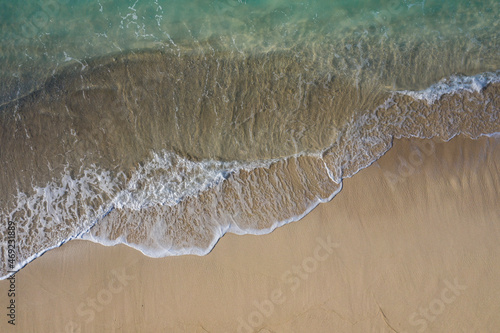 Aerial drone view in abstract mode of waves crashing along the shoreline of a white sand beach with turquoise clear lagoon water.