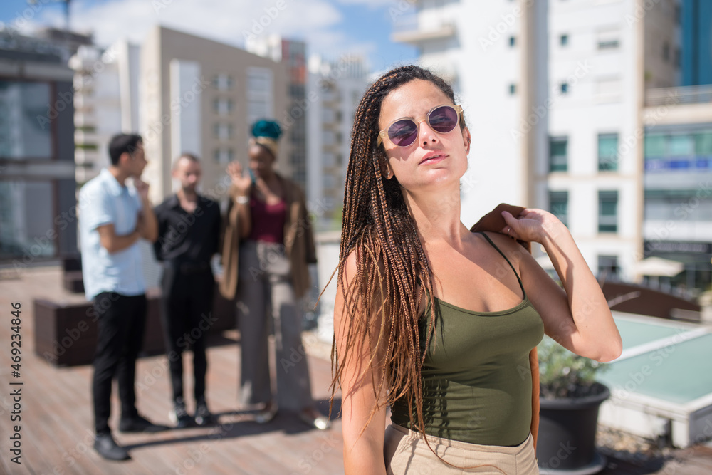Gorgeous caucasian woman on terrace roof party. Long-haired female in casual clothes and sunglasses. People of different nationalities standing in background. Teambuilding, party concept Gorgeous caucasian woman on terrace roof party. Long-haired female in casual clothes and sunglasses. People of different nationalities standing in background. Teambuilding, party concept