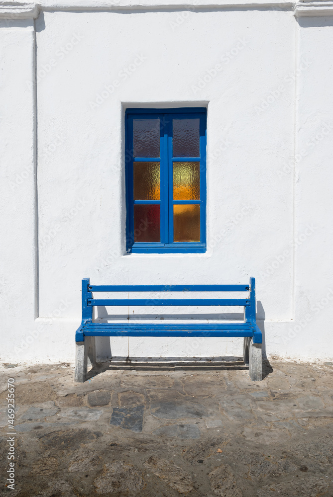 Blue bench under window against whitewashed wall in Mykonos, Greece.