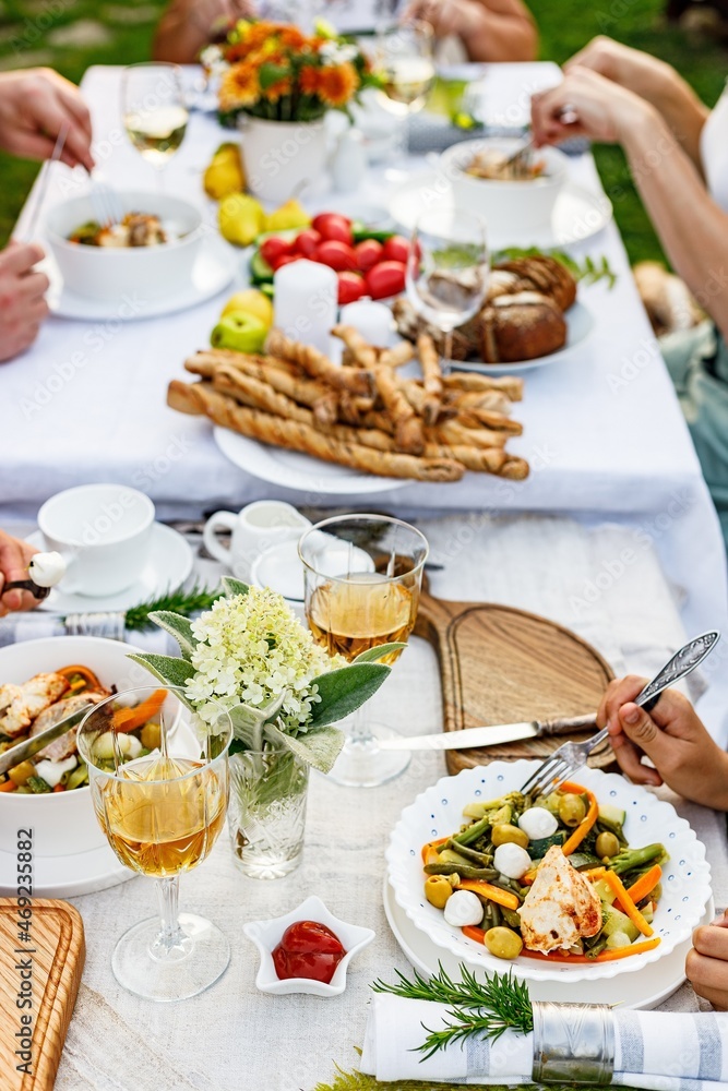 Family celebrations and food concept. The family is having dinner at a summer garden party. Table setting and decoration. Food and drinks. BBQ, vegetables, wine and other snacks. Life in the suburbs