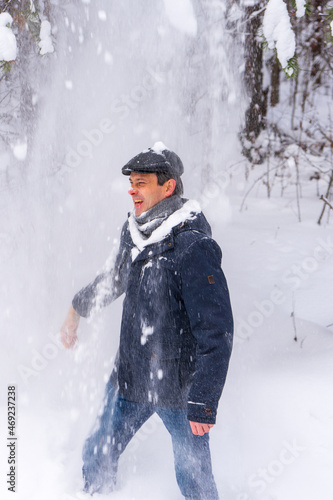 Portrait of middle-aged man having fun while shaking snow from tree branches in winter forest after snowfall. Winter holidays, active leisure, weekend trip to countryside concept