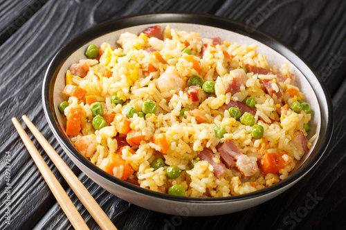 Yangzhou stir fried rice with egg and vegetables such as carrots, peas as well as shrimps, meat close up in the plate on the table. Horizontal