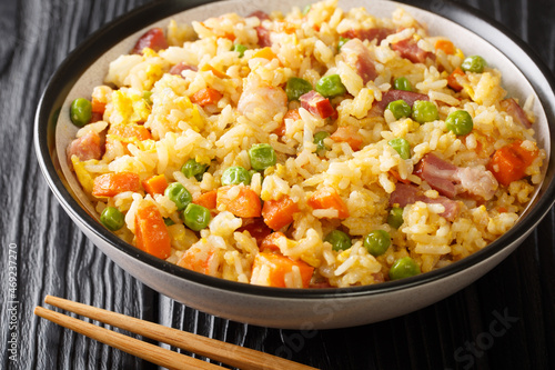 Yangzhou fried rice is a Chinese dish consisting of rice, egg and vegetables such as carrots, peas as well as shrimps, meat close up in the plate on the table. Horizontal