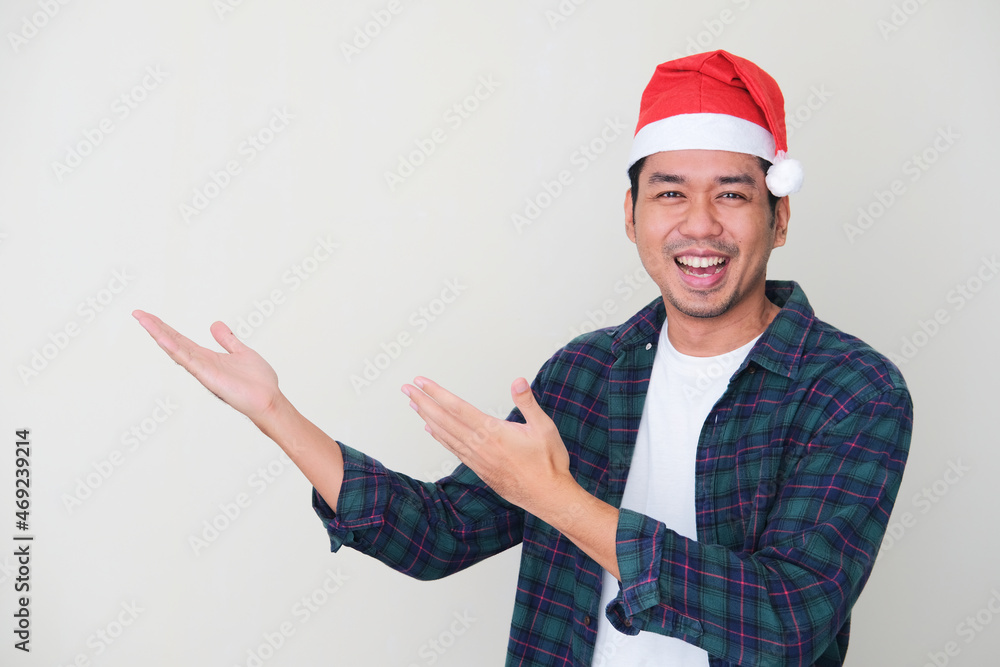 Adult Asian man wearing christmas hat smiling happy while showing beside Adult Asian man wearing christmas hat smiling happy while showing beside