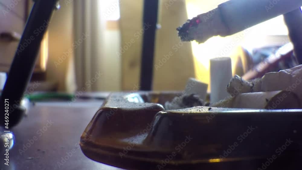 Ashing a cigarette into a ash tray on the table inside the living room of a house. Ashing a cigarette into a ash tray on the table inside the living room of a house.