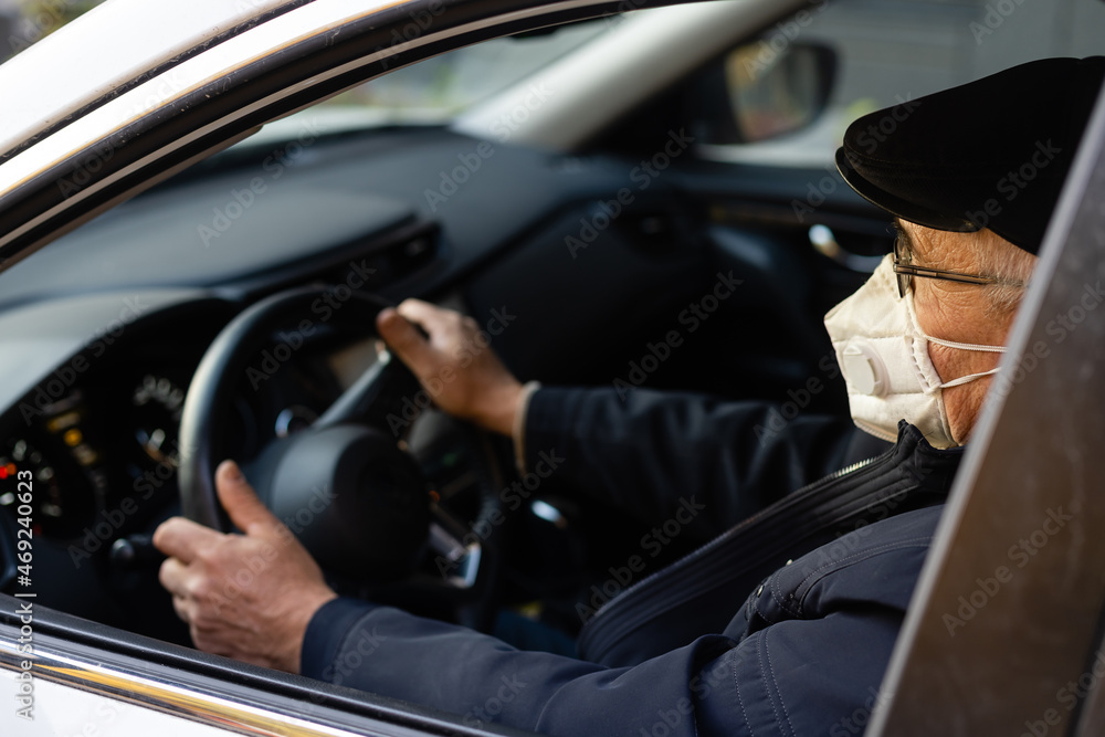 Elderly man wearing face mask entering his car at home.