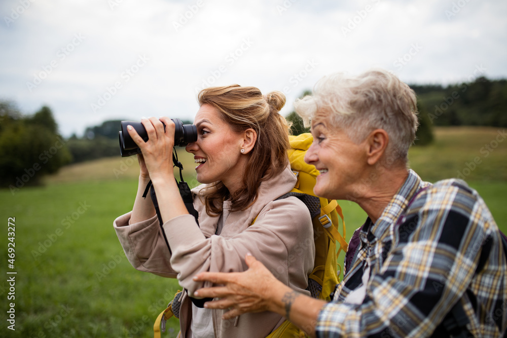 Happy senior mother hiker with adult daughter looking through binoculars outdoors in nature