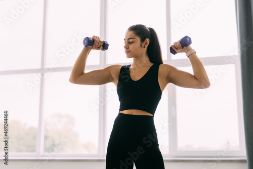 Young smiling young woman with dumbbells exercising at home