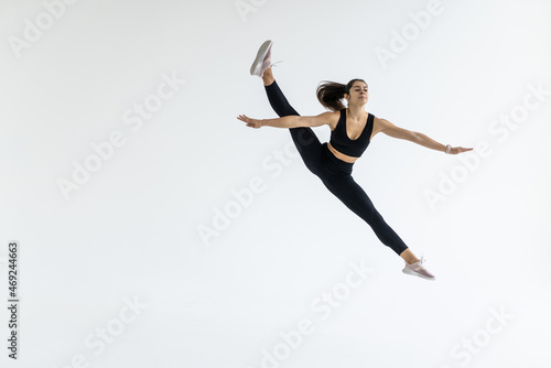 The portrait of beautiful young brunette woman gymnast training calilisthenics exercise with acrobatic element on white studio background. Art gymnastics concept. © F8  \ Suport Ukraine