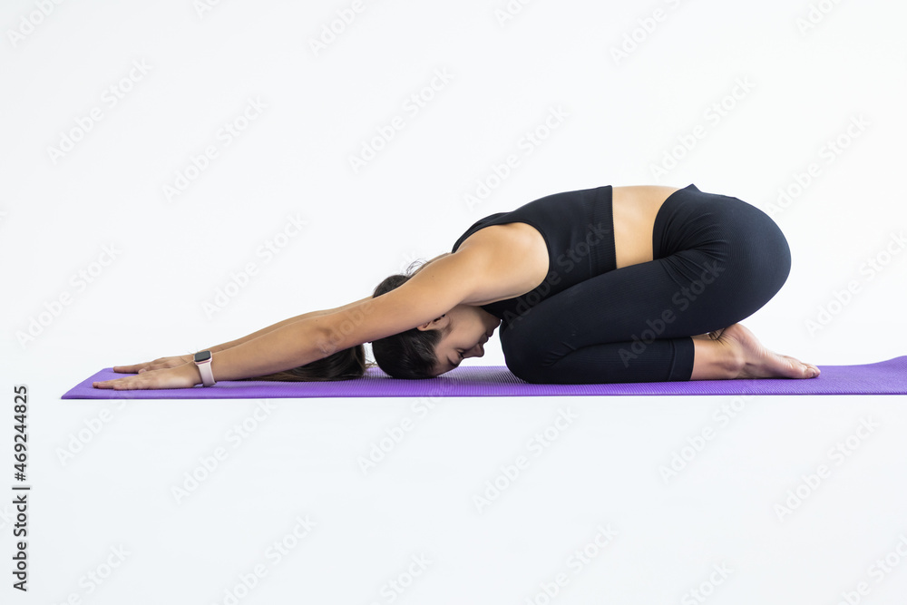 Young attractive woman practicing yoga, sitting in Child exercise, Balasana pose, working out wearing sportswear, white pants isolated against grey studio background