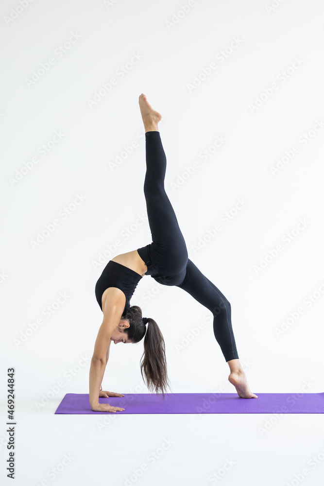 Young attractive woman practicing yoga, standing in Bridge exercise, One legged Wheel pose, working out wearing sportswear, white pants, indoor full length, isolated on white background