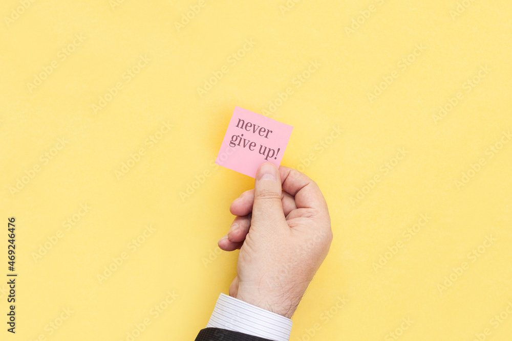 The hand holds a sticky note with inscription Never give up The hand holds a sticky note with inscription Never give up