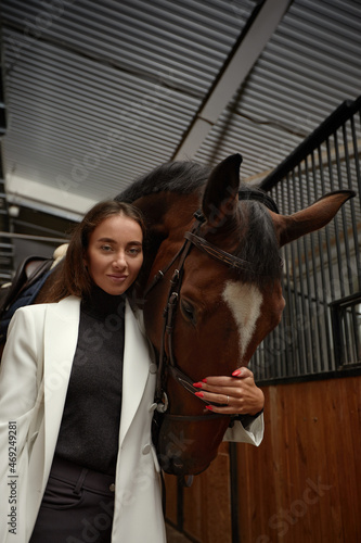 Portrait of smiling female jockey standing by horse in stable